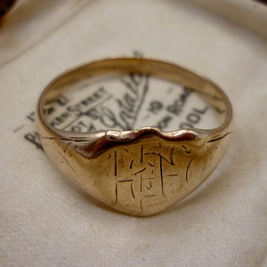 Könnte beinhalten: Ein goldener Siegelring mit einer Inschrift auf der Vorderseite. Der Ring befindet sich in einer Samtbox.