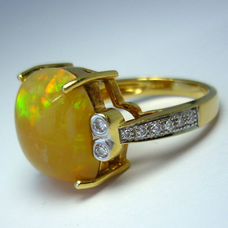 May include: A gold ring with a large, round, yellow opal gemstone set in a prong setting. The ring has a band of smaller diamonds set in a pave setting.