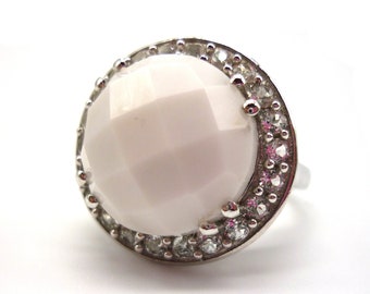 May include: A white gemstone ring with a faceted center stone surrounded by a halo of smaller clear stones.