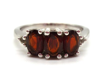 May include: A silver ring with three oval-shaped red gemstones set in a prong setting.