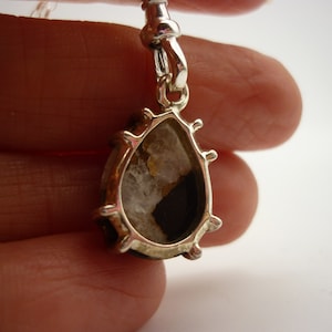 May include: Silver pendant with a teardrop-shaped clear stone with brown and white inclusions. The stone is set in a silver bezel with a decorative edge.