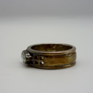 May include: A silver ring with a clear stone and a geometric design on the band.