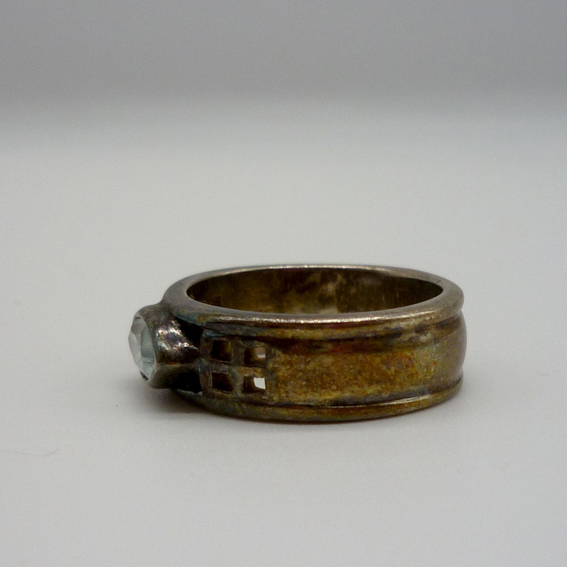 May include: A silver ring with a clear stone and a geometric design on the band.