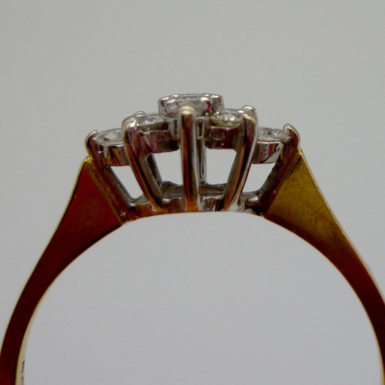 May include: Close-up of a gold ring with a cluster of three diamonds. The diamonds are set in a white metal, and the band is gold. The ring is set against a plain white background.