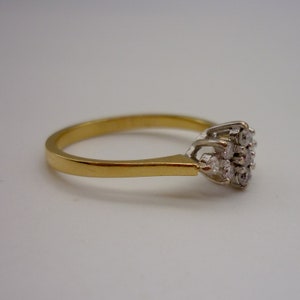 May include: A gold ring with a cluster of small diamonds. The ring has a thin gold band and a white gold setting for the diamonds. The diamonds are arranged in a floral pattern.
