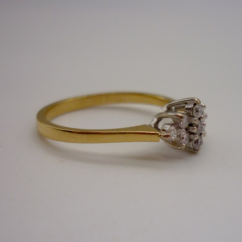 May include: A gold ring with a cluster of small diamonds. The ring has a thin gold band and a white gold setting for the diamonds. The diamonds are arranged in a floral pattern.
