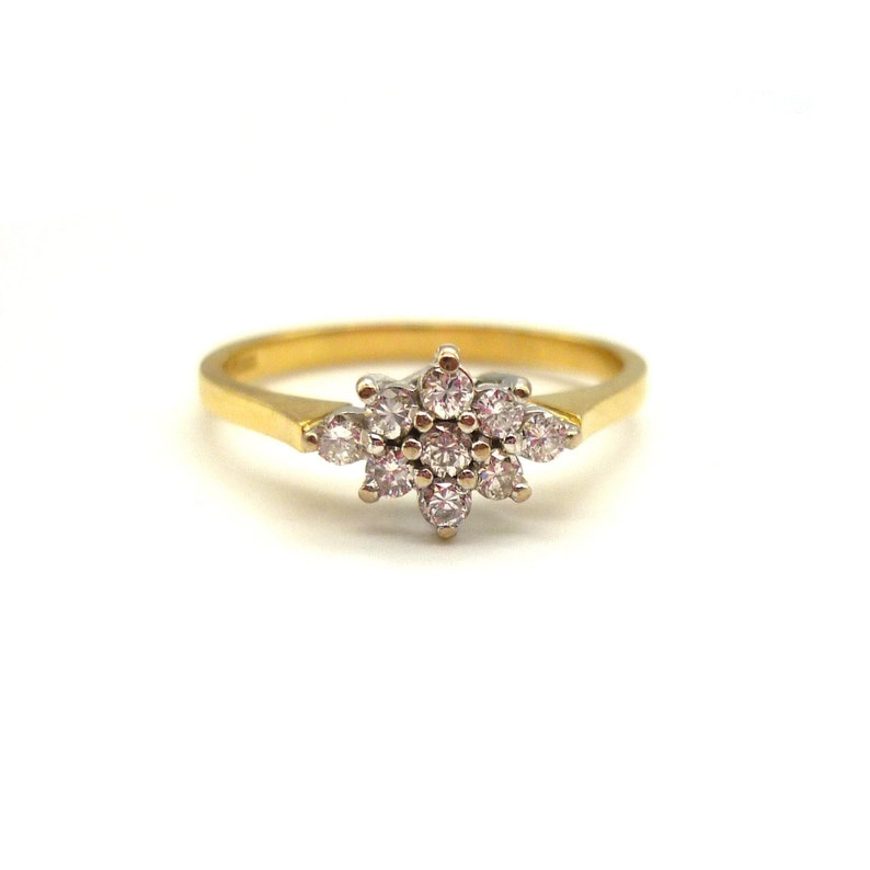 May include: A gold ring featuring a cluster of small, round, clear gemstones arranged in a floral pattern. The ring has a thin, gold band and a white metal setting for the gemstones.