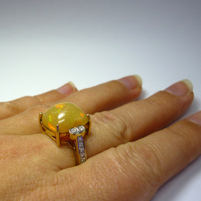 May include: A gold ring with a large yellow opal gemstone and smaller diamond accents. The ring is set on a finger.