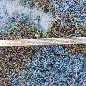 May include: A gold tie bar with a geometric pattern. The tie bar is lying on a bed of moss.
