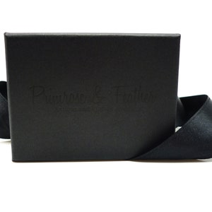May include: A black box with a black ribbon tied around it. The box has the text "Primrose & Feather" embossed on the front.