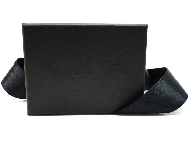 May include: A black box with a black ribbon tied around it. The box has the text "Primrose & Feather" embossed on the front.