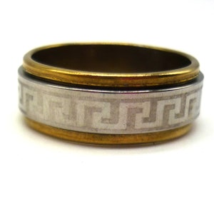May include: A gold and silver ring with a Greek key design. The ring is made of metal and has a polished finish.