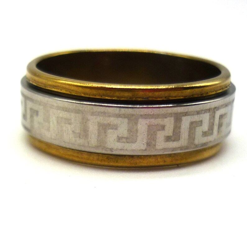 May include: A gold and silver ring with a Greek key design. The ring is made of metal and has a polished finish.