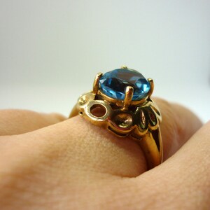 May include: A gold ring with a large blue gemstone. The ring has a detailed design with intricate details.