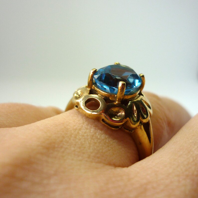May include: A gold ring with a large blue gemstone. The ring has a detailed design with intricate details.