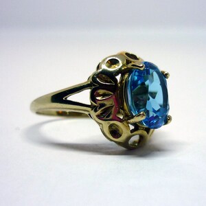 May include: A gold ring with a blue topaz gemstone set in a decorative filigree design.