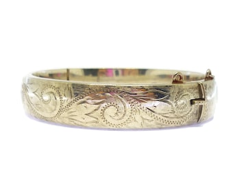 Könnte beinhalten: Ein goldenes Armreif-Armband mit einem zarten Blumenmuster. Das Armband ist aus Metall und hat einen Scharnierverschluss.
