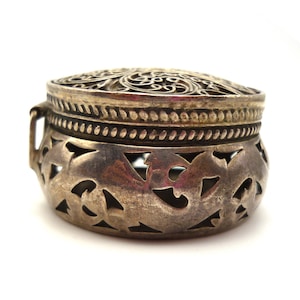 May include: A silver trinket box with an intricate, cut-out design. The box has a round shape and a hinged lid.