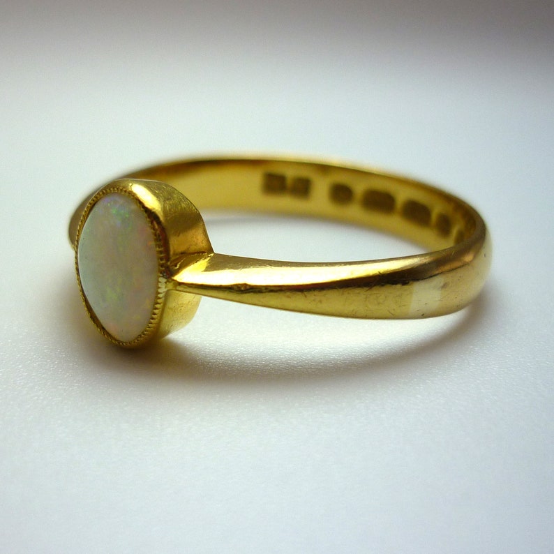 May include: A gold ring with a white opal gemstone. The ring has a simple band and the opal is set in a bezel.