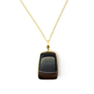 May include: A gold chain necklace with a black and white agate pendant. The pendant is rectangular and has a smooth, polished finish.