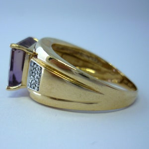 May include: A gold ring featuring a large, square, purple gemstone and a row of smaller, white gemstones on the band.