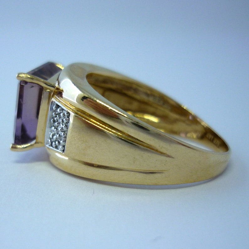 May include: A gold ring featuring a large, square, purple gemstone and a row of smaller, white gemstones on the band.