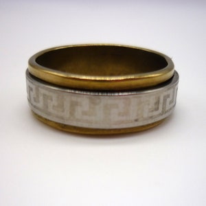 May include: A gold and silver ring with a geometric pattern. The ring is made of two bands, one gold and one silver, that are joined together. The silver band has a geometric pattern that is etched into the metal.