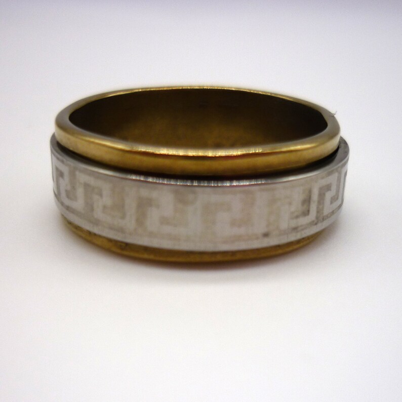 May include: A gold and silver ring with a geometric pattern. The ring is made of two bands, one gold and one silver, that are joined together. The silver band has a geometric pattern that is etched into the metal.