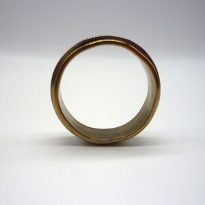 May include: A gold-toned ring with a smooth, polished finish. The ring is made of two different metals, with a silver band on the inside and a gold band on the outside.