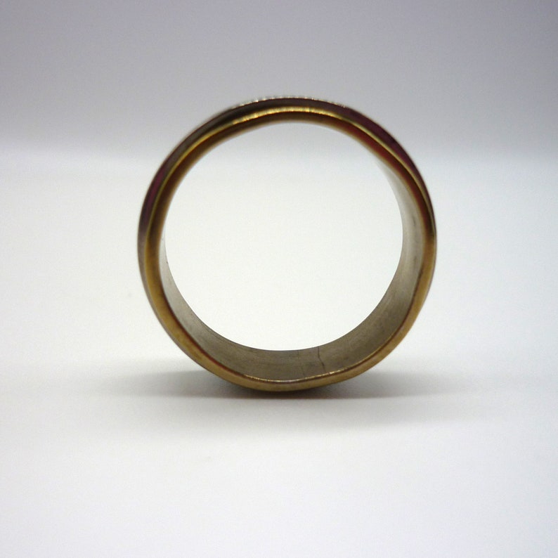 May include: A gold-toned ring with a smooth, polished finish. The ring is made of two different metals, with a silver band on the inside and a gold band on the outside.