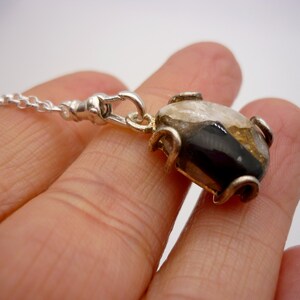 May include: A silver chain necklace with a pendant featuring a black, white, and gold stone set in a silver frame.