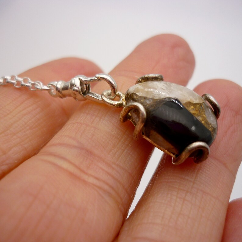 May include: A silver chain necklace with a pendant featuring a black, white, and gold stone set in a silver frame.
