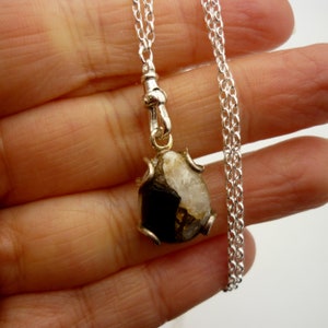 May include: A silver chain necklace with a pendant featuring a black and white gemstone set in a silver frame.