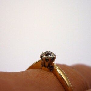 May include: A gold ring with a single, clear diamond set in a prong setting.