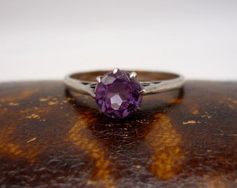 May include: A silver ring with a purple gemstone set in a prong setting.