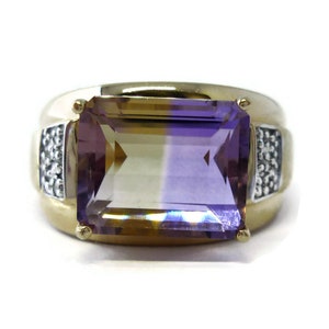 May include: A gold ring featuring a large, rectangular, bi-coloured gemstone. The gemstone is a light yellow on the top half and a purple on the bottom half. The ring is accented with small diamonds on the sides.