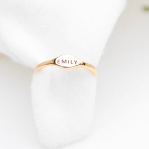 May include: A gold ring with a flat oval-shaped top that says "EMILY" in all caps.