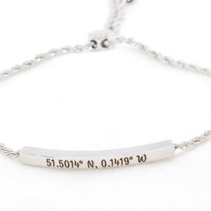 May include: A silver bracelet with a rope chain and a silver bar charm engraved with the coordinates "51.5014° N, 0.1419° W".