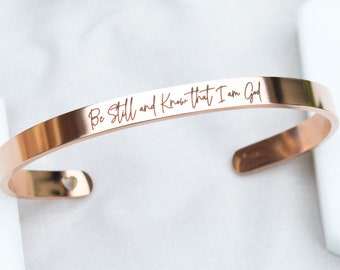 May include: Rose gold bangle bracelet with the inscription "Be Still and Know that I am God".