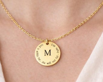 Op de afbeelding: Een goudkleurige ketting met een ronde hanger met in het midden de letter M en de gegraveerde tekst God is within her, she will not fall - Psalm 46:5. De hanger hangt aan een fijne goudkleurige ketting met kleine, ronde schakels.