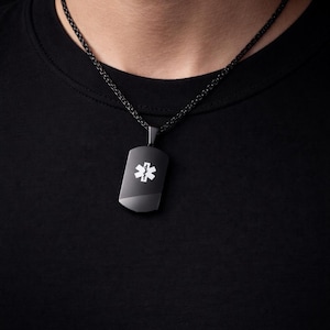 Peut inclure: Un pendentif de plaque d'identité médicale noir suspendu à une chaîne noire assortie. Le pendentif rectangulaire présente un symbole blanc de l'Étoile de Vie avec un emblème central de serpent et de bâton, servant d'identification médicale.