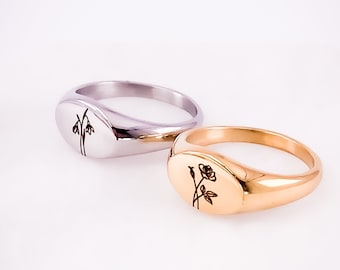 May include: Two signet rings with engraved floral designs. The ring on the left is silver with a snowdrop flower design. The ring on the right is gold with a rose design.