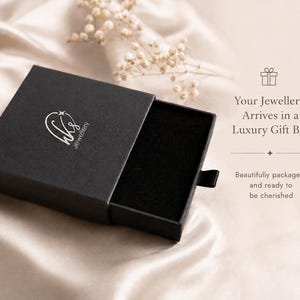 May include: A black rectangular sliding jewelry gift box with a silver logo featuring the letters wks and a star. The box has a black velvet interior lining. Text on the right reads: Your Jewellery Arrives in a Luxury Gift Box.