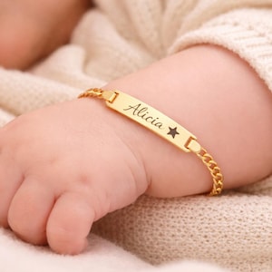 May include: A gold-toned metal identification bracelet featuring a flat rectangular bar engraved with the name Alicia and a small star symbol. The bracelet is constructed with a delicate curb chain link design and a secure clasp mechanism.