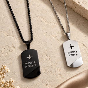 May include: Two dog tag pendants on chains. The black pendant features a four-pointed star and the coordinates 40.7128° N 74.0060° W. The silver pendant features a four-pointed star and the coordinates 51.5074° N 0.1278° W. Both have a diagonal accent.