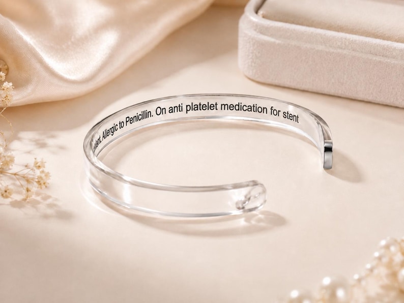 May include: A clear, open-ended cuff bracelet featuring black engraved text on the inner surface that reads: Allergic to Penicillin. On anti platelet medication for stent. The bracelet has a smooth, polished finish and a simple, circular design.