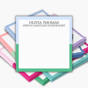 May include: A stack of colorful notepads with white pages. The top notepad is divided vertically, with a light blue and green section. Text on the top notepad reads "OLIVIA THOMAS SPEECH LANGUAGE PATHOLOGIST."