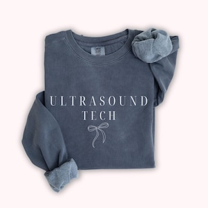 May include: A dark blue sweatshirt with the text "ULTRASOUND TECH" and a small white bow design.