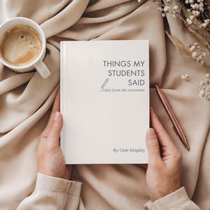 May include: A white book titled "THINGS MY STUDENTS SAID" with a pencil illustration and the subtitle "Tales from the classroom". A cup of coffee and a pen are next to the book on a beige surface.