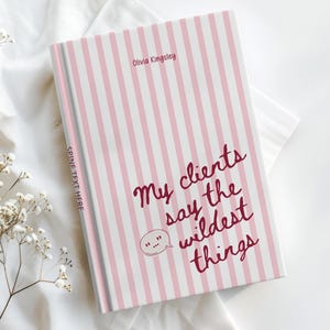 May include: A hardcover book with a light pink and white vertical striped cover. The text on the front reads Olivia Kingsley and My clients say the wildest things with a speech bubble icon. The spine text reads SPINE TEXT HERE.